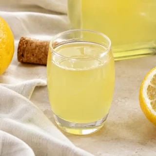 Glass of Homemade Limoncello served chilled with fresh lemons and a bottle in the background.