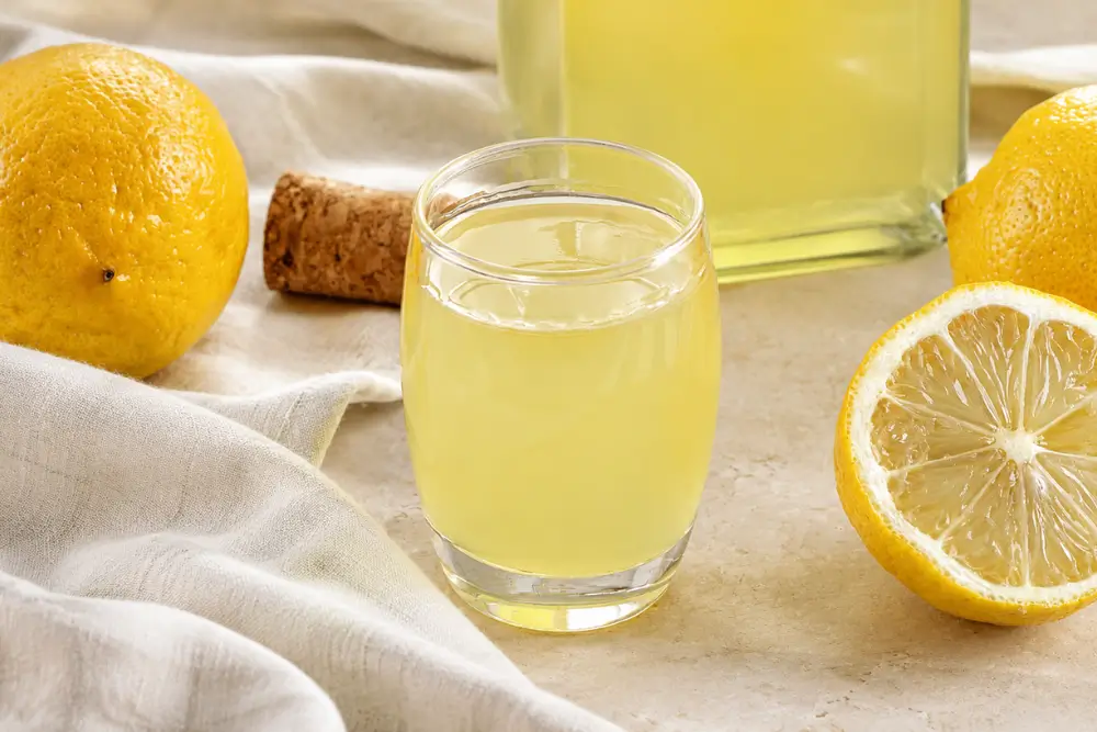 Glass of Homemade Limoncello served chilled with fresh lemons and a bottle in the background.