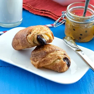 Finished pain au chocolat with flaky layers and dark chocolate filling on a serving plate.