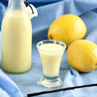 Small glass of Crema di Limoncello beside bottle and fresh lemons.