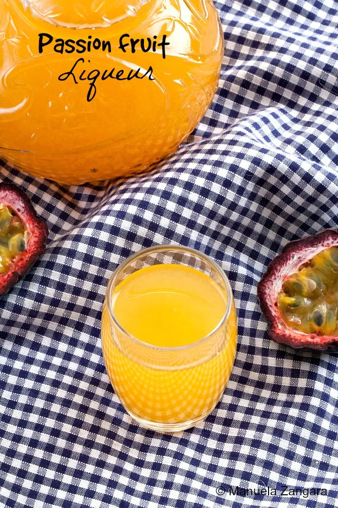 Glass of golden passion fruit liqueur with halved fruit on gingham cloth.