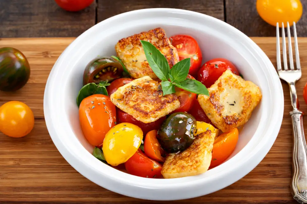 Halloumi and cherry tomatoes tossed together in a bowl with fresh basil.