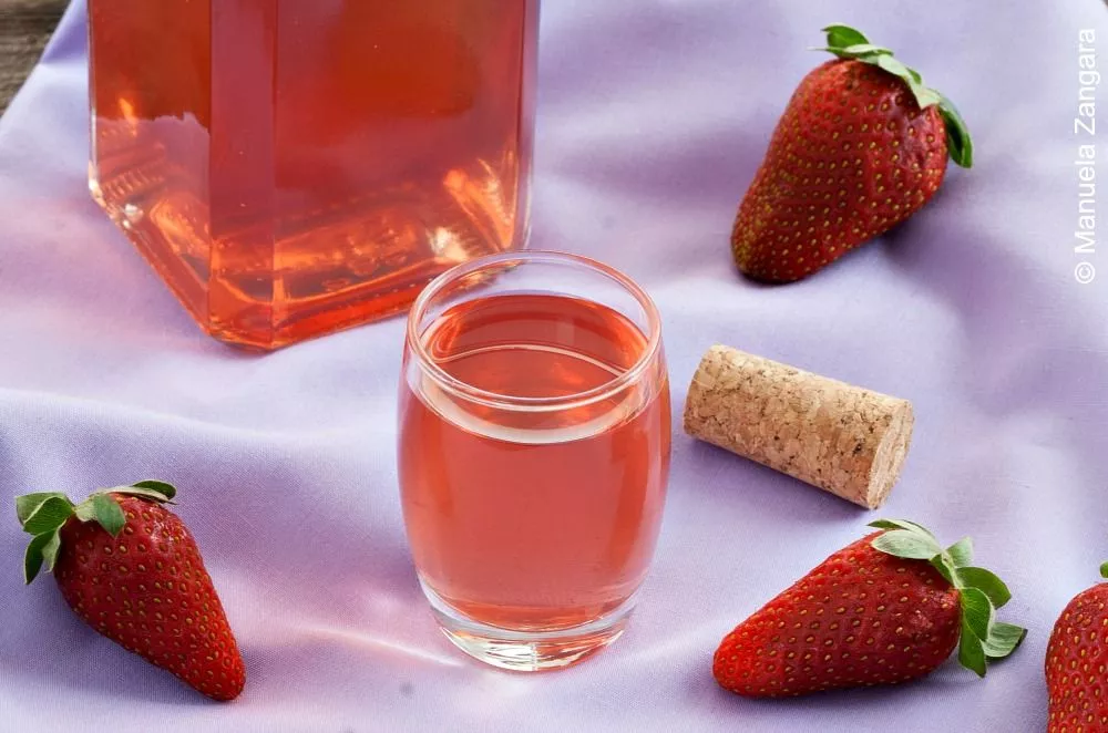 Homemade Fragolino strawberry liqueur displayed with fresh strawberries and a bottle in the background.