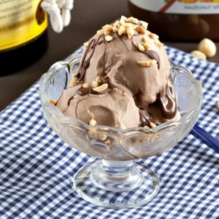 Creamy homemade hazelnut gelato in a glass bowl with chocolate drizzle and chopped nuts on top.
