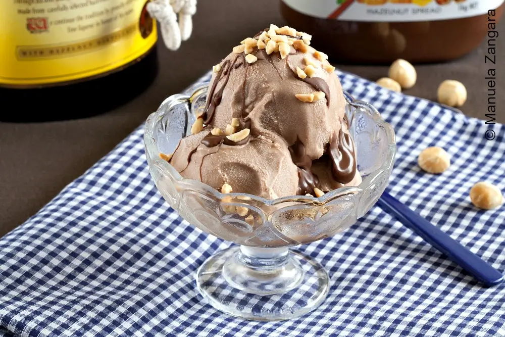 Creamy homemade hazelnut gelato in a glass bowl with chocolate drizzle and chopped nuts on top.