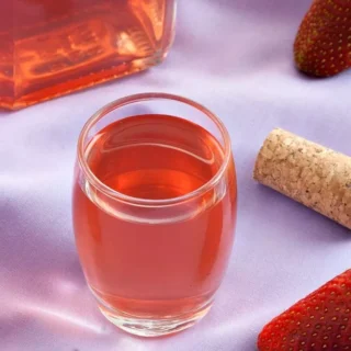Fragolino Liqueur in a clear glass with fresh strawberries and cork on a lilac cloth.