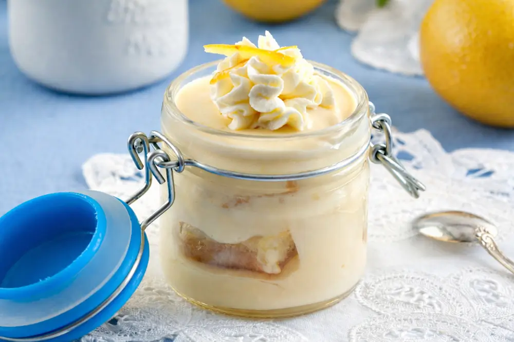 Creamy lemon dessert in a jar on a lace cloth with fresh lemons in the background.