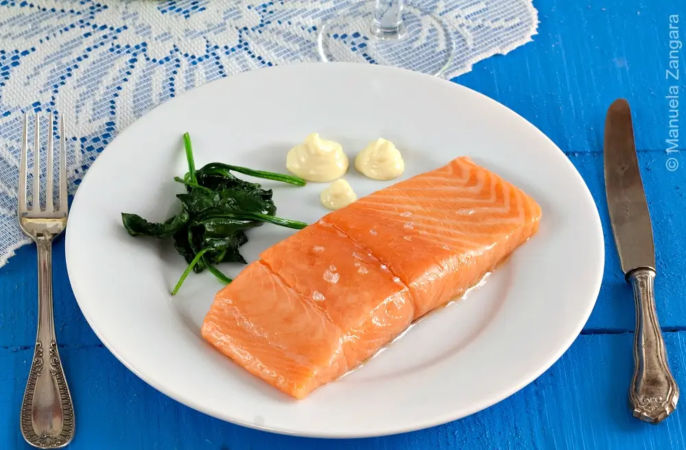 Poached salmon fillet served with aioli and sautéed spinach on a white plate.