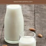Small glass of almond milk with whole almonds scattered on a wooden surface.