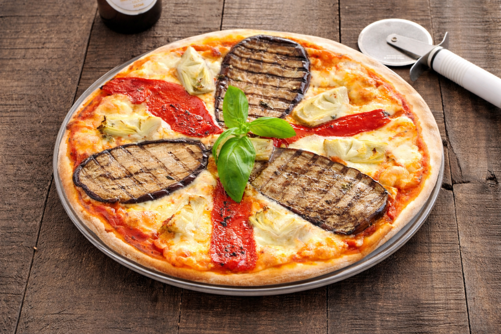 Ortolana pizza with grilled eggplant, roasted peppers, artichokes, and melted mozzarella on a wooden table.