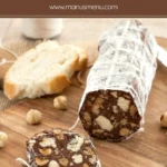 Salame di cioccolato log dusted with icing sugar and sliced on a wooden board with hazelnuts.