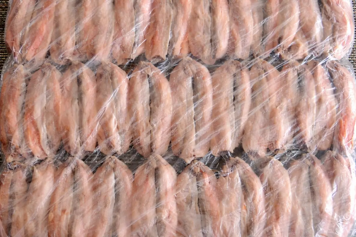 Anchovies arranged in rows and covered tightly with plastic wrap during marination.