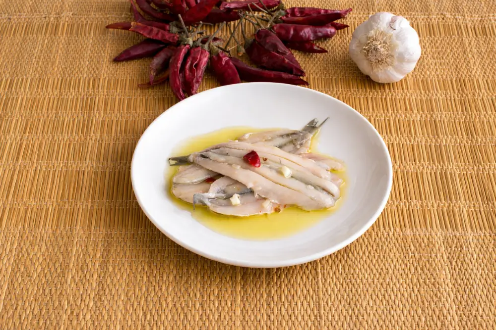 Anchovies plated with olive oil, garlic pieces, and chilli flakes.