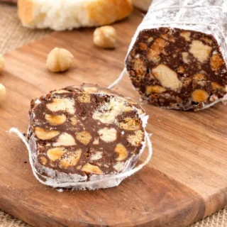 Slice of Chocolate Salami showing biscuit pieces and hazelnuts on a wooden board.