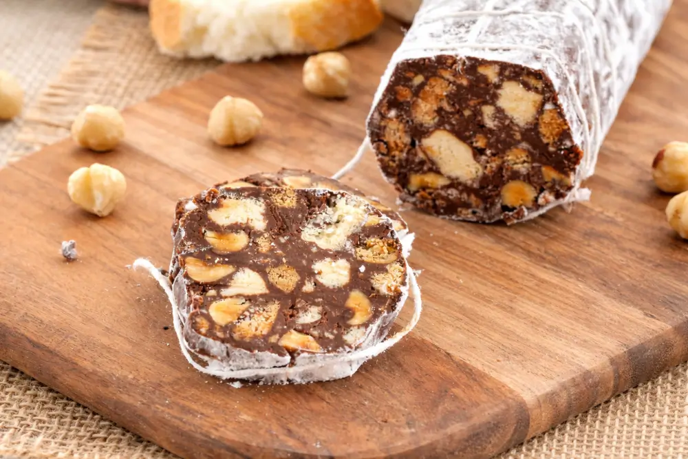 Slice of Chocolate Salami showing biscuit pieces and hazelnuts on a wooden board.