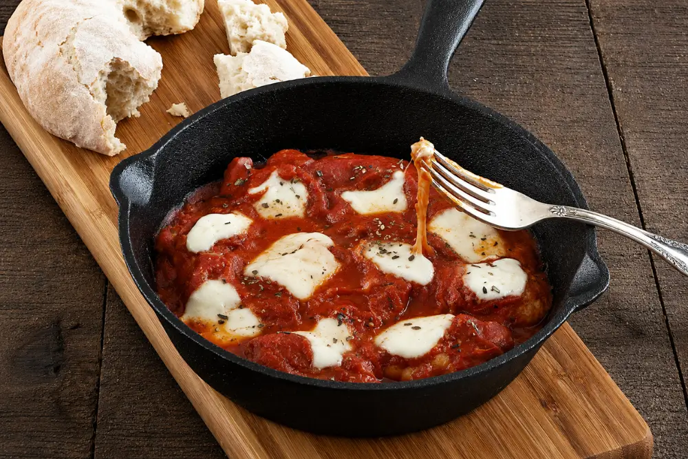 Fork lifting melted cheese from skillet chicken with tomato sauce and bocconcini.
