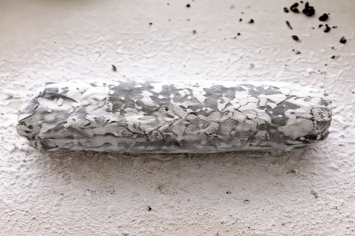 Whole chocolate biscuit salami log dusted with icing sugar on a wooden board.