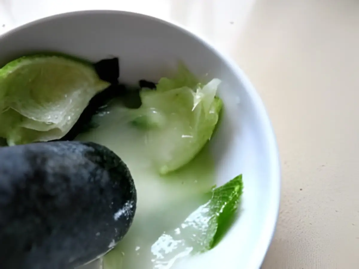 Muddling lime wedges and mint leaves in a bowl to release juice and aroma.