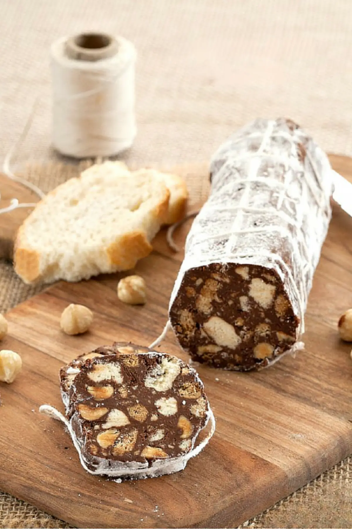 Salame di cioccolato log dusted with icing sugar and sliced on a wooden board with hazelnuts.