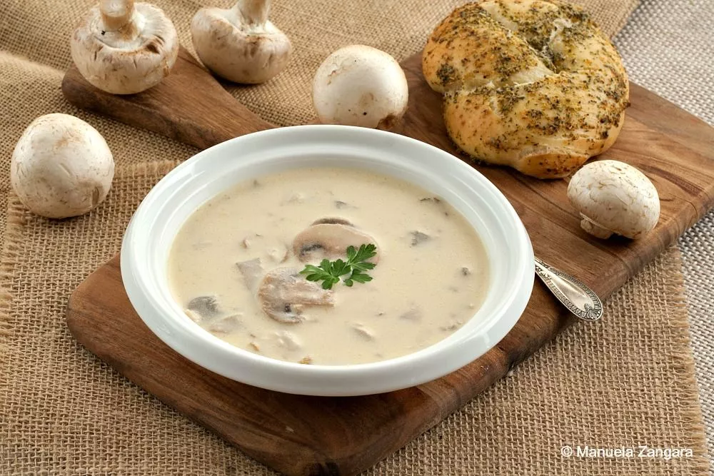 Creamy mushroom soup with fresh mushrooms and parsley, served in a white bowl.
