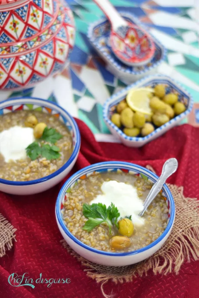 Warm Freekeh soup topped with yoghurt and parsley, served with olives and lemon.