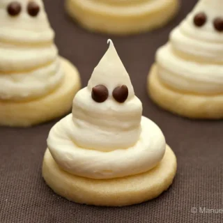 Close-up of Halloween ghost cookies made with buttery shortbread and whipped white chocolate ganache, decorated with chocolate chip eyes.