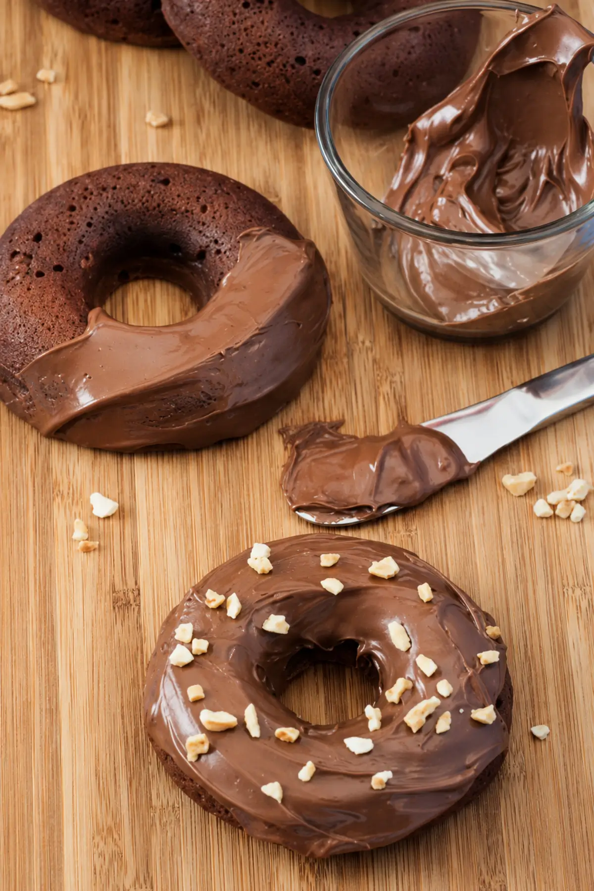 Nutella doughnut topped with chocolate-hazelnut spread and chopped hazelnuts on a wooden board.