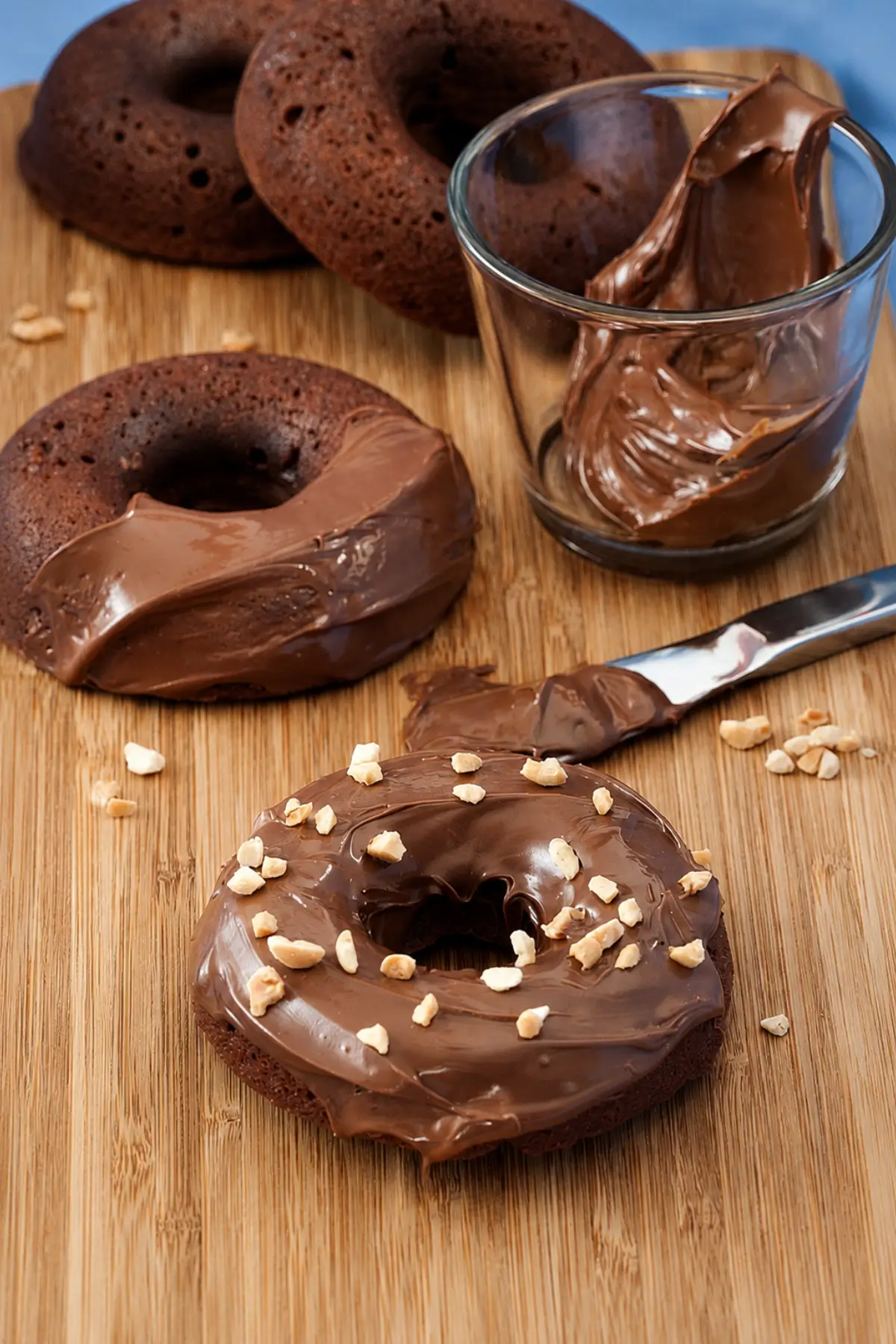 Mini Nutella doughnuts topped with Nutella glaze and chopped hazelnuts on a wooden board.