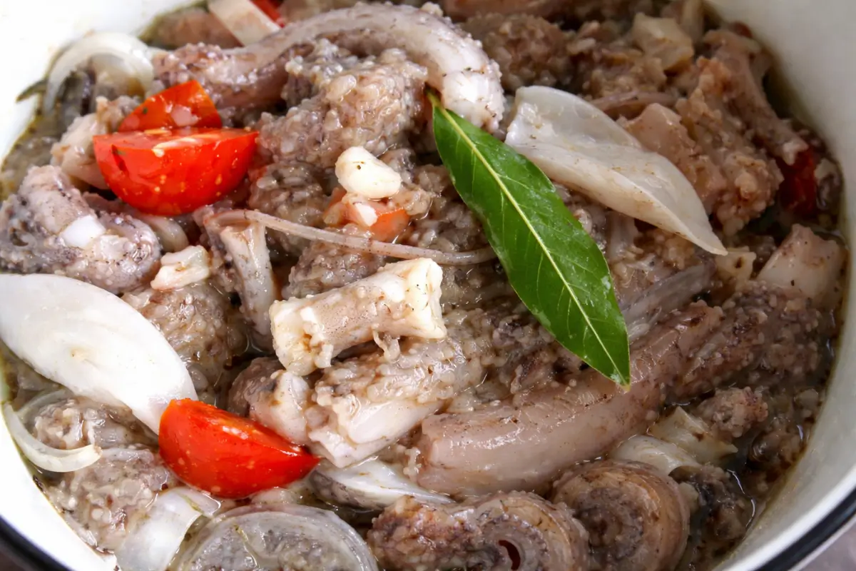 Octopus cooking in a pot with cherry tomatoes and bay leaves.