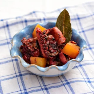 Polipo accupatello served in a small bowl with tender octopus, potatoes, and a bay leaf garnish.