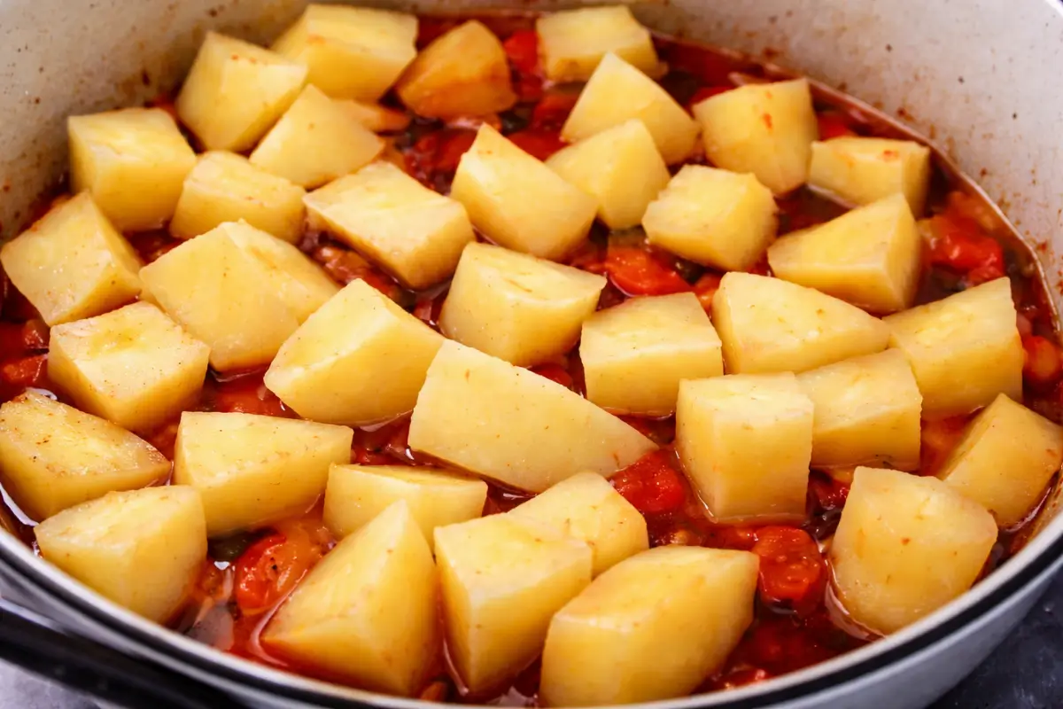 Cubed potatoes added to a tomato-based octopus stew simmering in a pan.