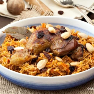 Kabsa rice with chicken drumstick, almonds, and raisins served on a woven mat.