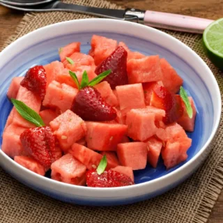 Watermelon and Strawberry Salad with Ginger and Lime Syrup served in a blue bowl with fresh mint and lime.