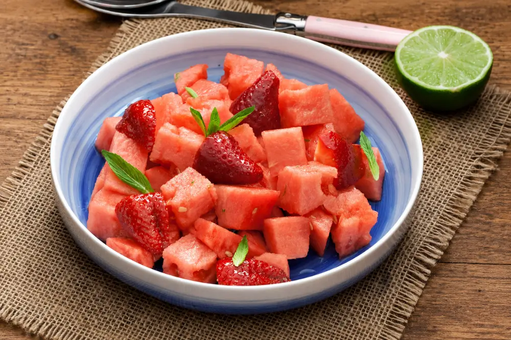 Watermelon and Strawberry Salad with Ginger and Lime Syrup served in a blue bowl with fresh mint and lime.