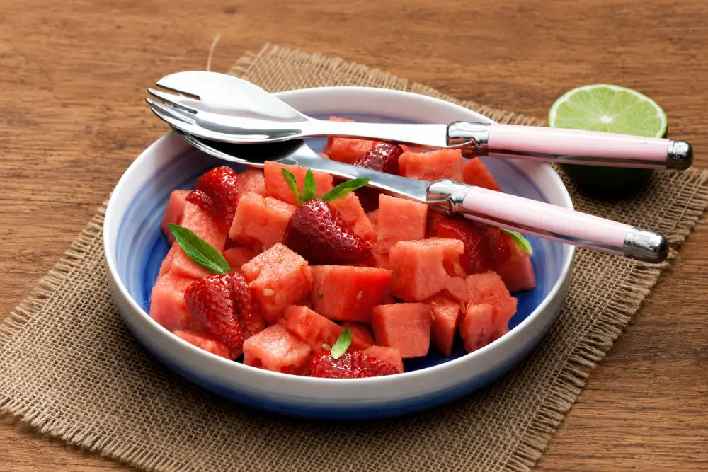 Watermelon salad with strawberries, mint leaves, and lime served chilled in a blue bowl.
