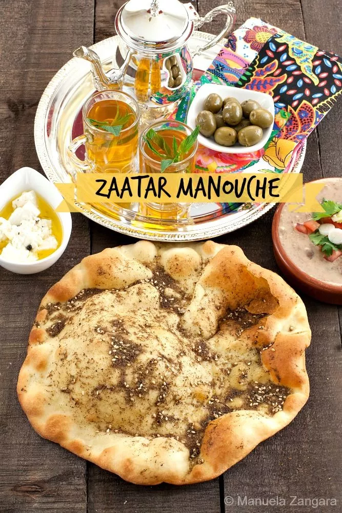 Zaatar Manouche flatbread served with olives, mint tea, and cheese on a wooden table.