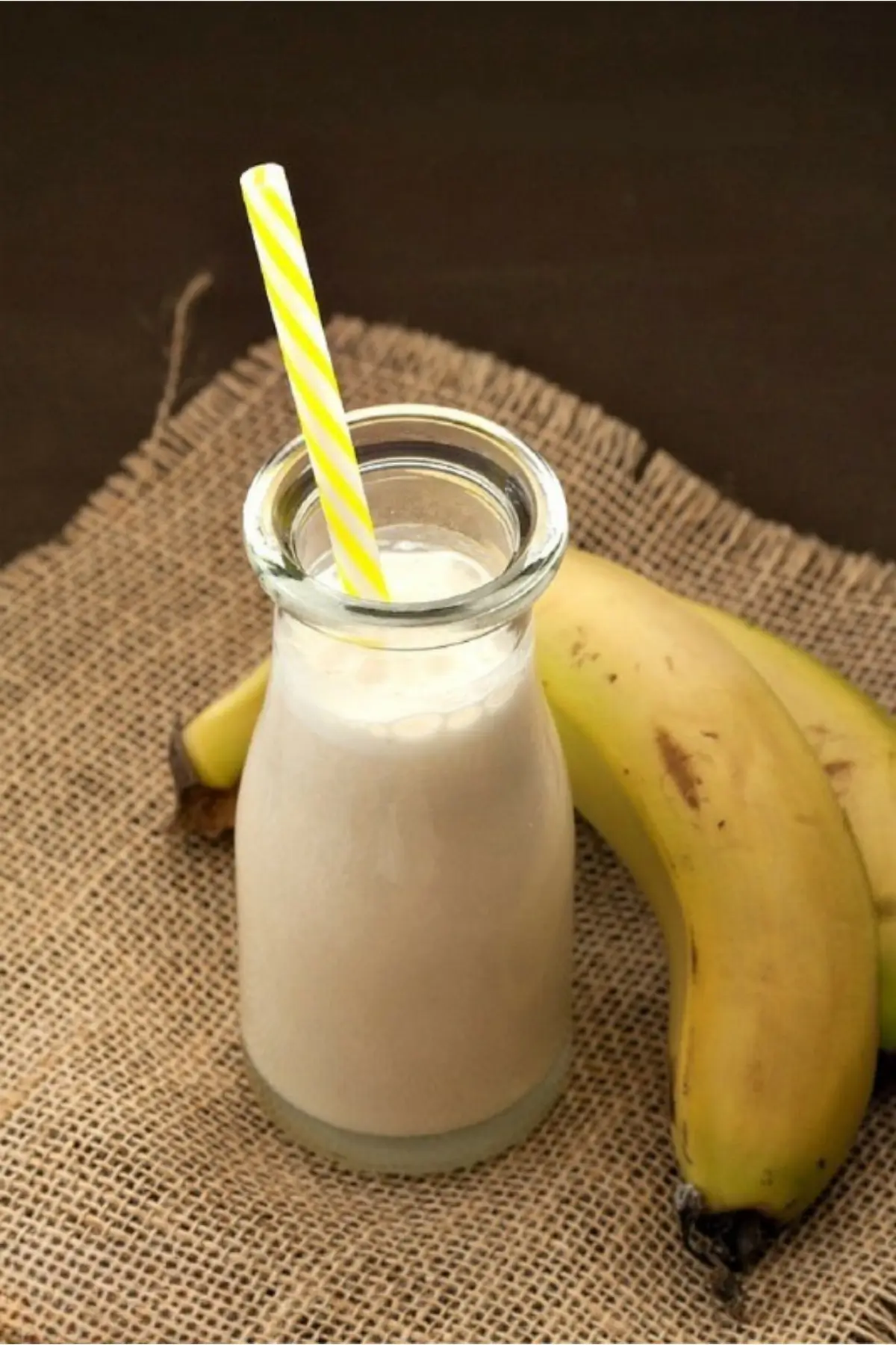 Homemade banana milk served in a small glass bottle with a striped straw.