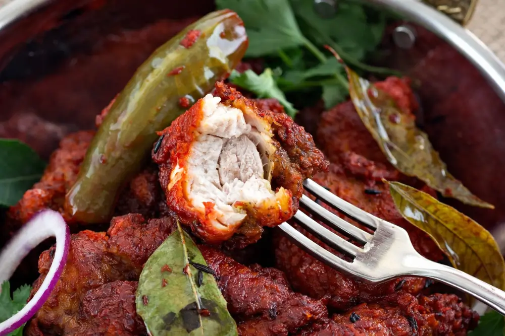 Chicken 65 with tender white interior, coated in red chilli spices and served with curry leaves and green chilli.