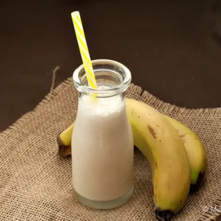 Freshly blended banana drink in a glass bottle with a straw.