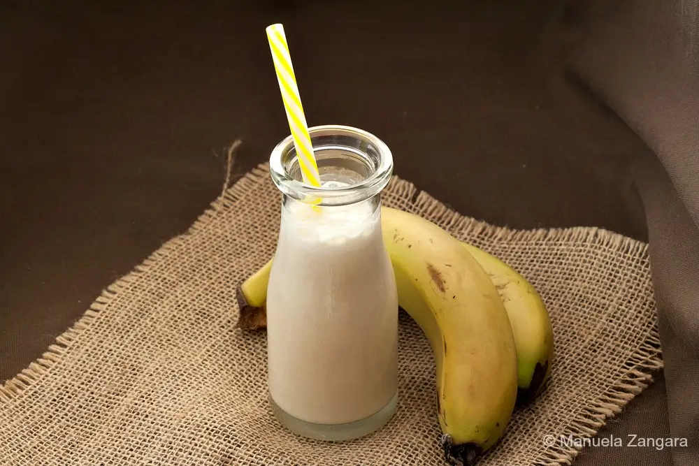 Freshly blended banana drink in a glass bottle with a straw.