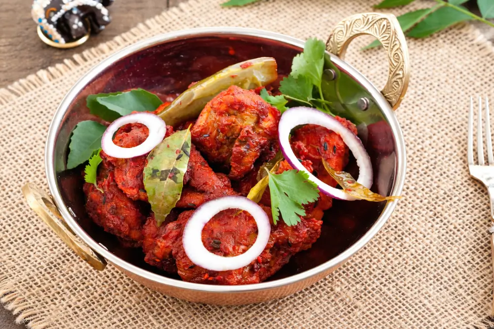 Bowl of deep-fried red chicken garnished with onion rings, green chillies and curry leaves.