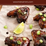Baked glazed chicken wings arranged on a serving board with lime wedges and spring onions.