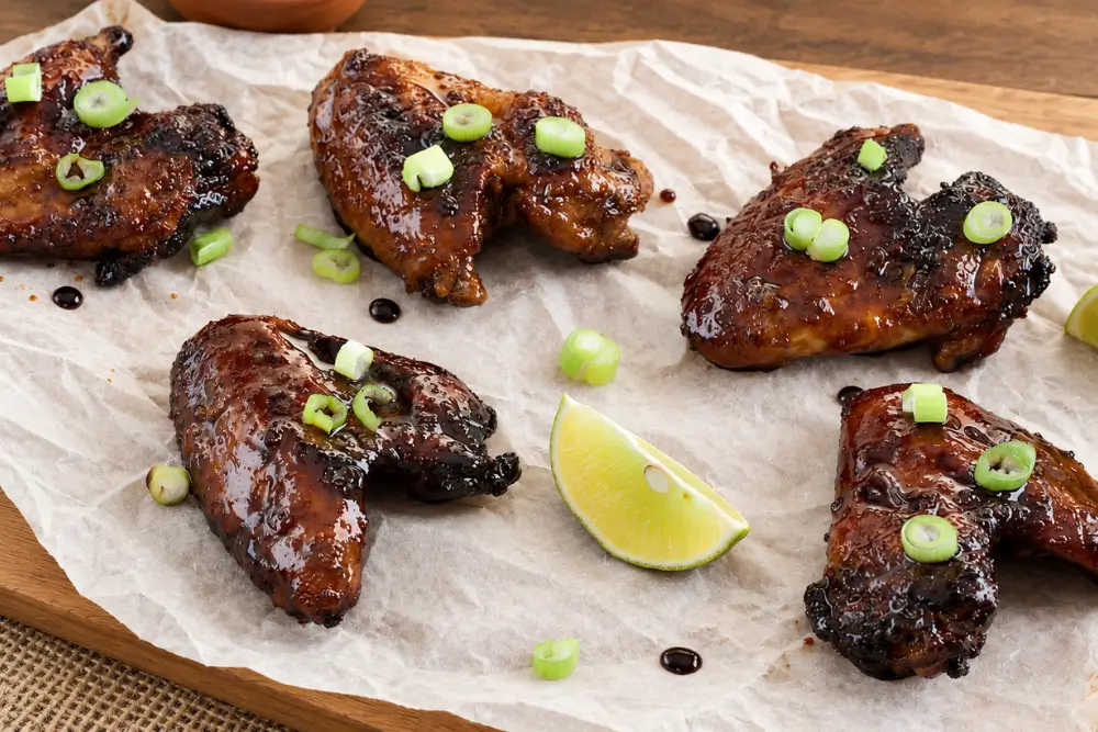 Baked glazed chicken wings arranged on a serving board with lime wedges and spring onions.