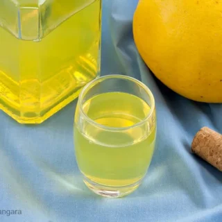Bottle and glass of grapefruit liqueur arranged on blue cloth with a grapefruit.