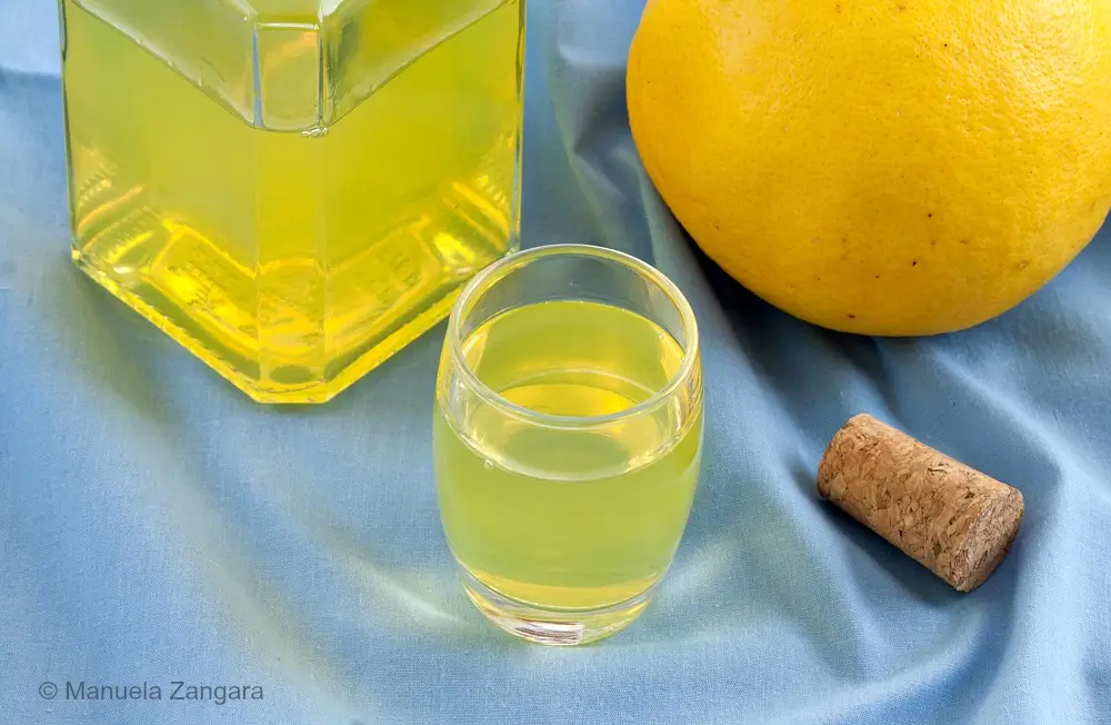 Bottle and glass of grapefruit liqueur arranged on blue cloth with a grapefruit.