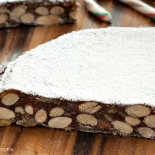 Slices of Panforte dusted with icing sugar on a wooden board with a candy cane.