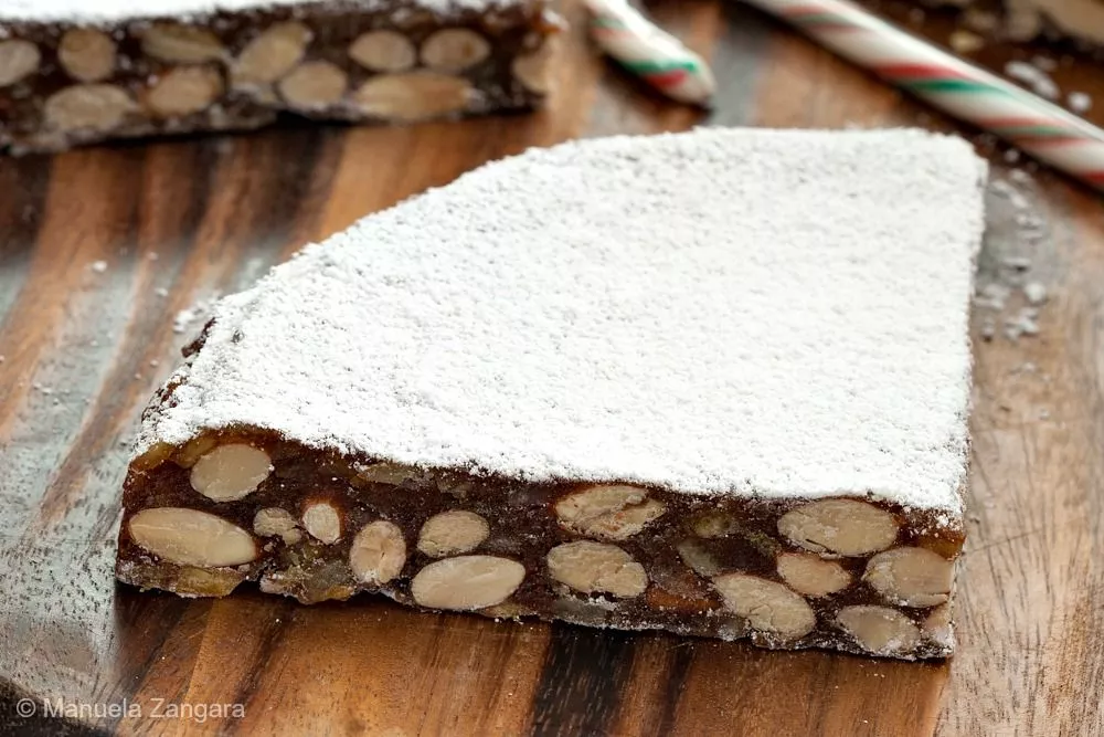 Slices of Panforte dusted with icing sugar on a wooden board with a candy cane.