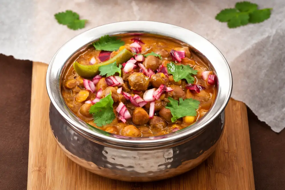 Close-up of chole masala topped with onions, cilantro, and lime wedge.