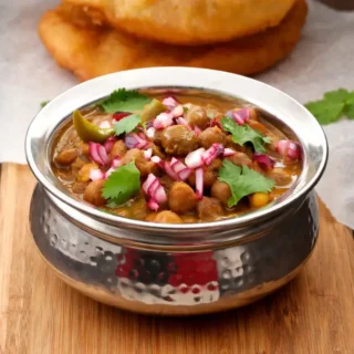 Chole masala served in a metal bowl with bhatura and fresh coriander garnish.