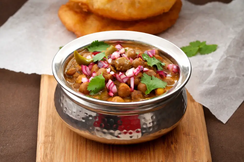 Chole masala served in a metal bowl with bhatura and fresh coriander garnish.